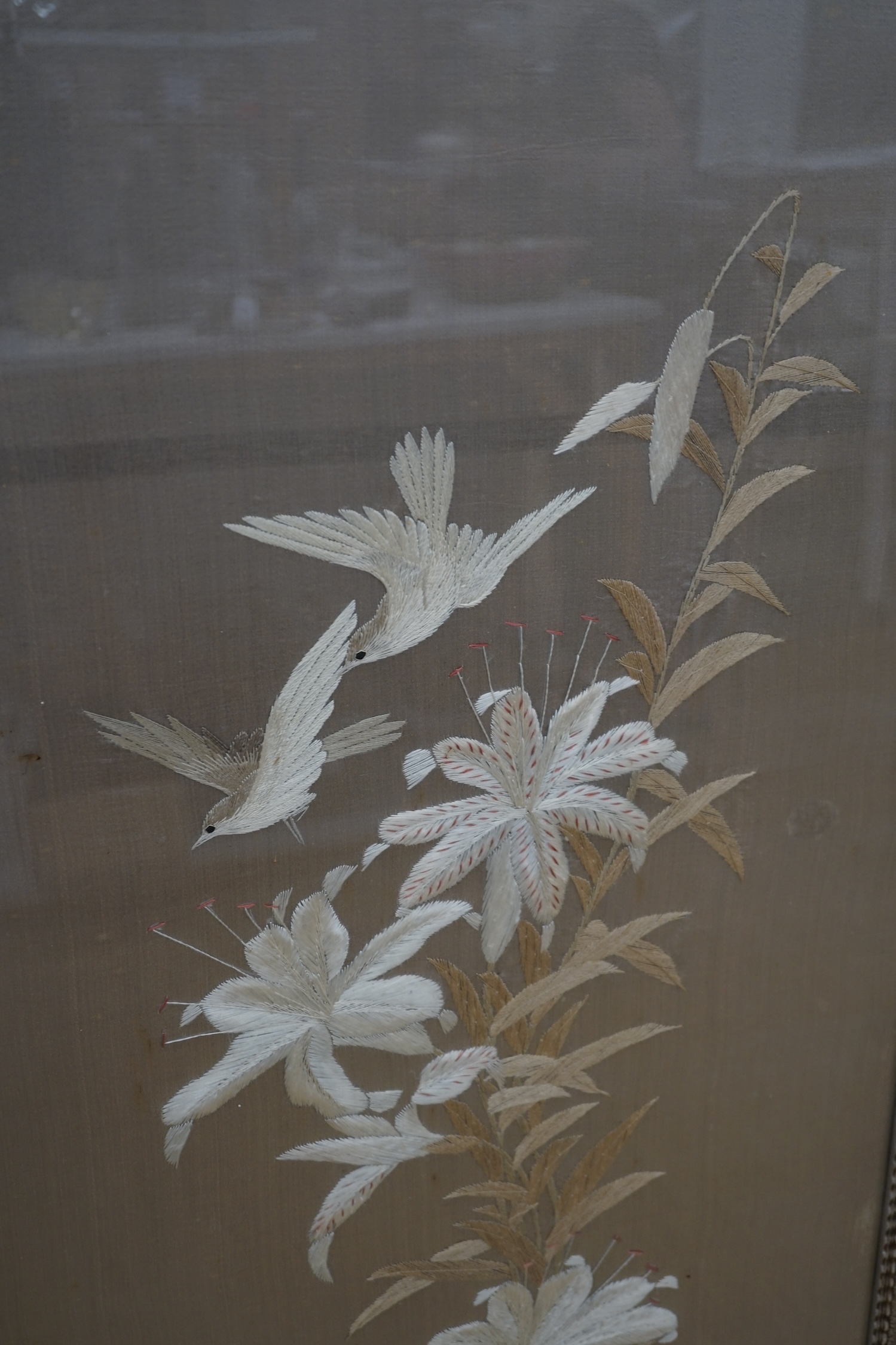 A 1900 to 1920’s Japanese silk embroidery of birds in flight and flowers on a grey background, 131cm high, 52cm wide, together with a Japanese silk and metallic thread still life embroidery on black background, with couc